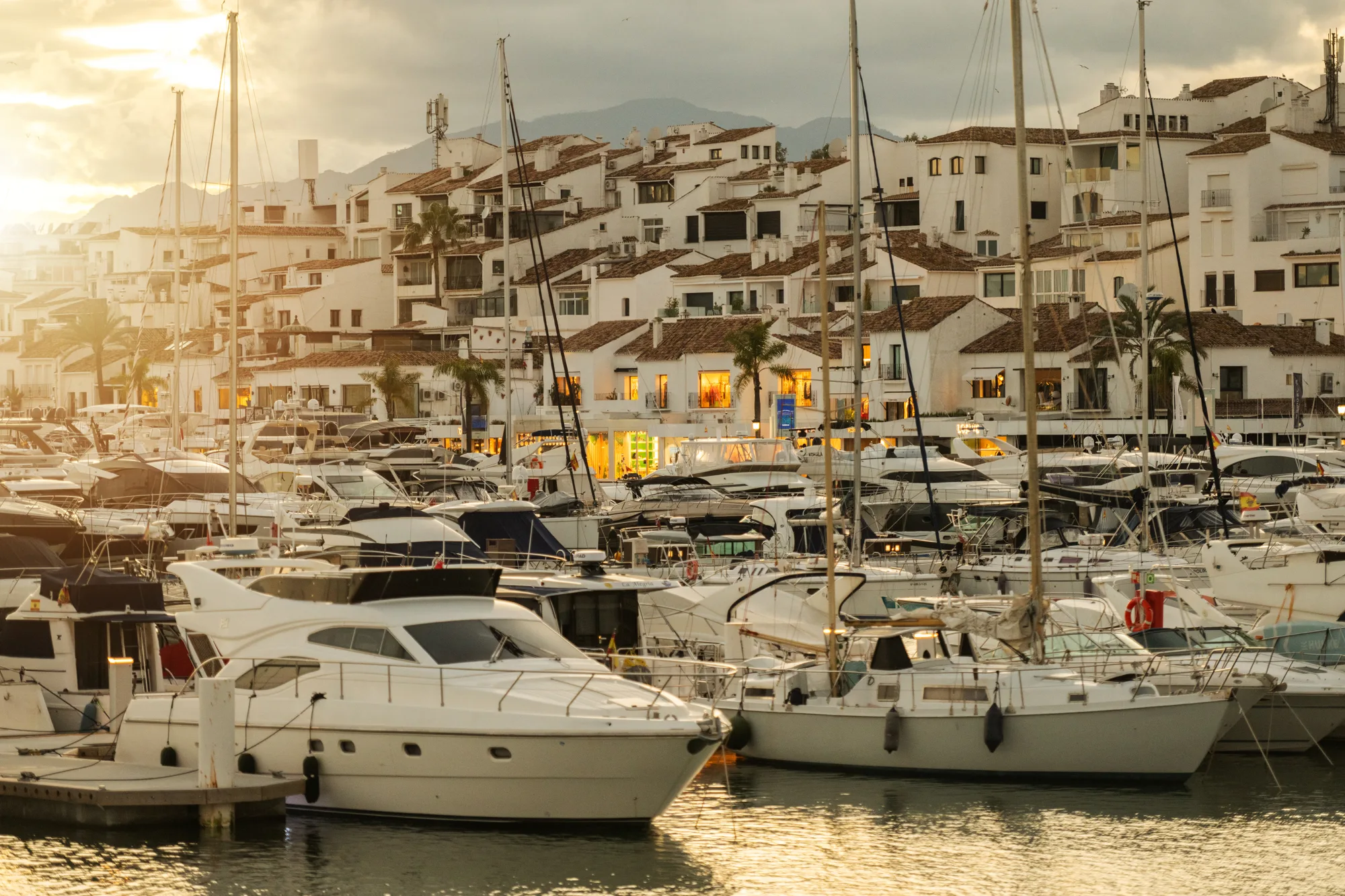 Jahte i gliseri privezani u marini Puerto Banús, iza njih bele zgrade marine u kasnopopodnevnom svetlu
