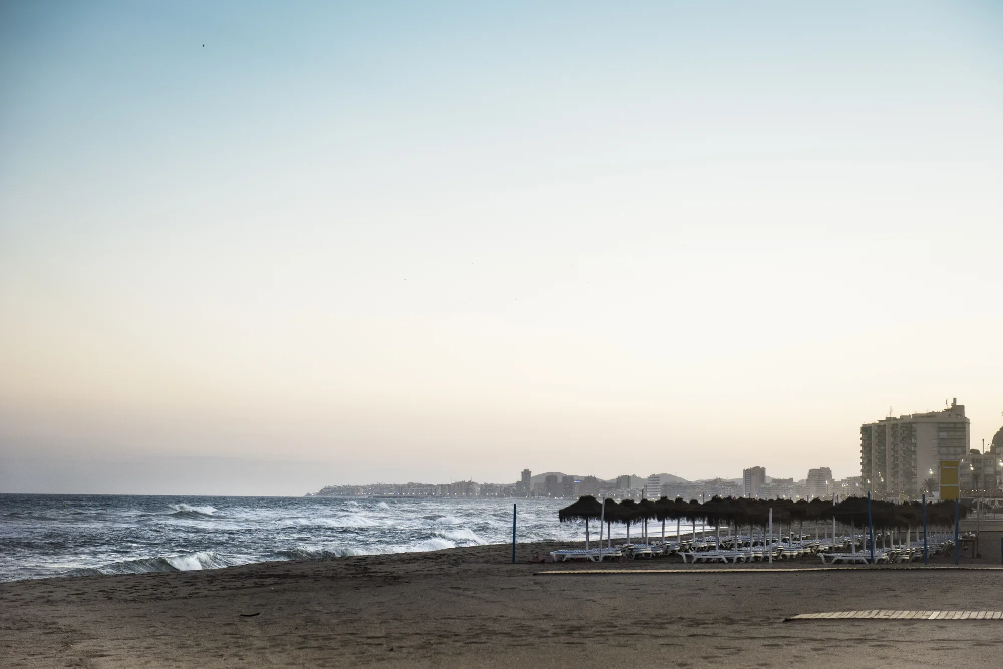 Ležaljke i suncobrani od trske na plaži Torreblanca u Fuengiroli rano ujutru, bez gužve, sa zgradama uz obalu