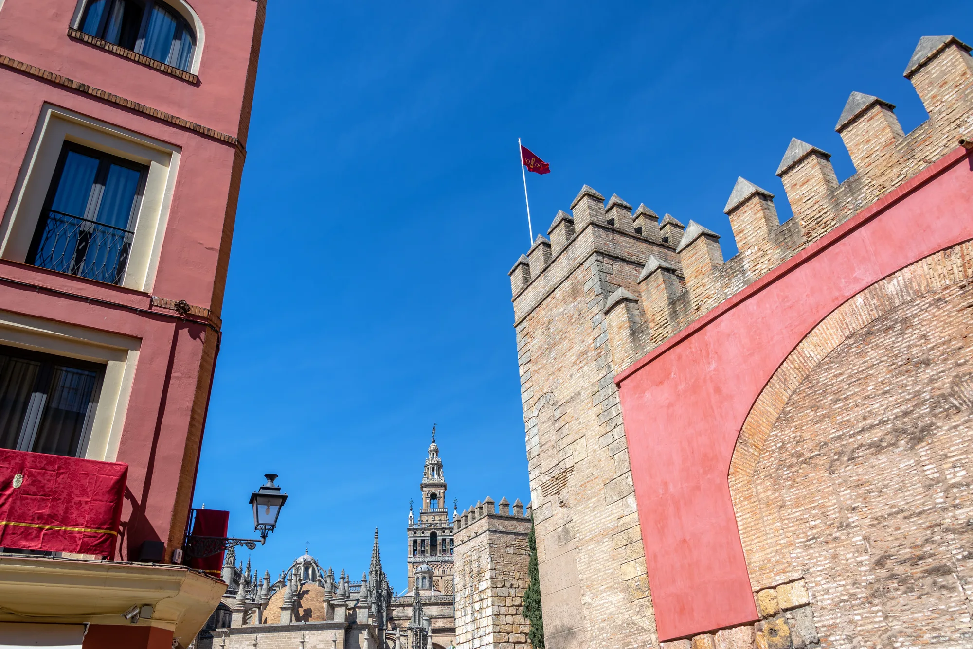 Crveni zid sa lučnom kapijom Puerta del León i kule zidina Alkazara, u pozadini zvonik Giralda