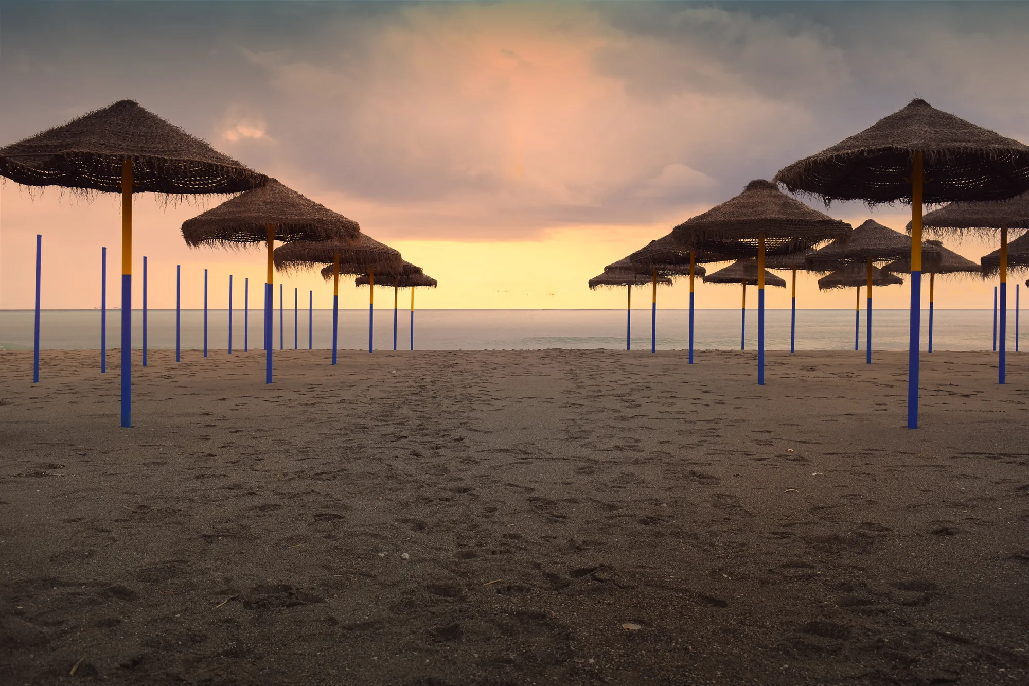 Prazna peščana plaža u Benalmádeni sa suncobranima od trske u zalazak sunca