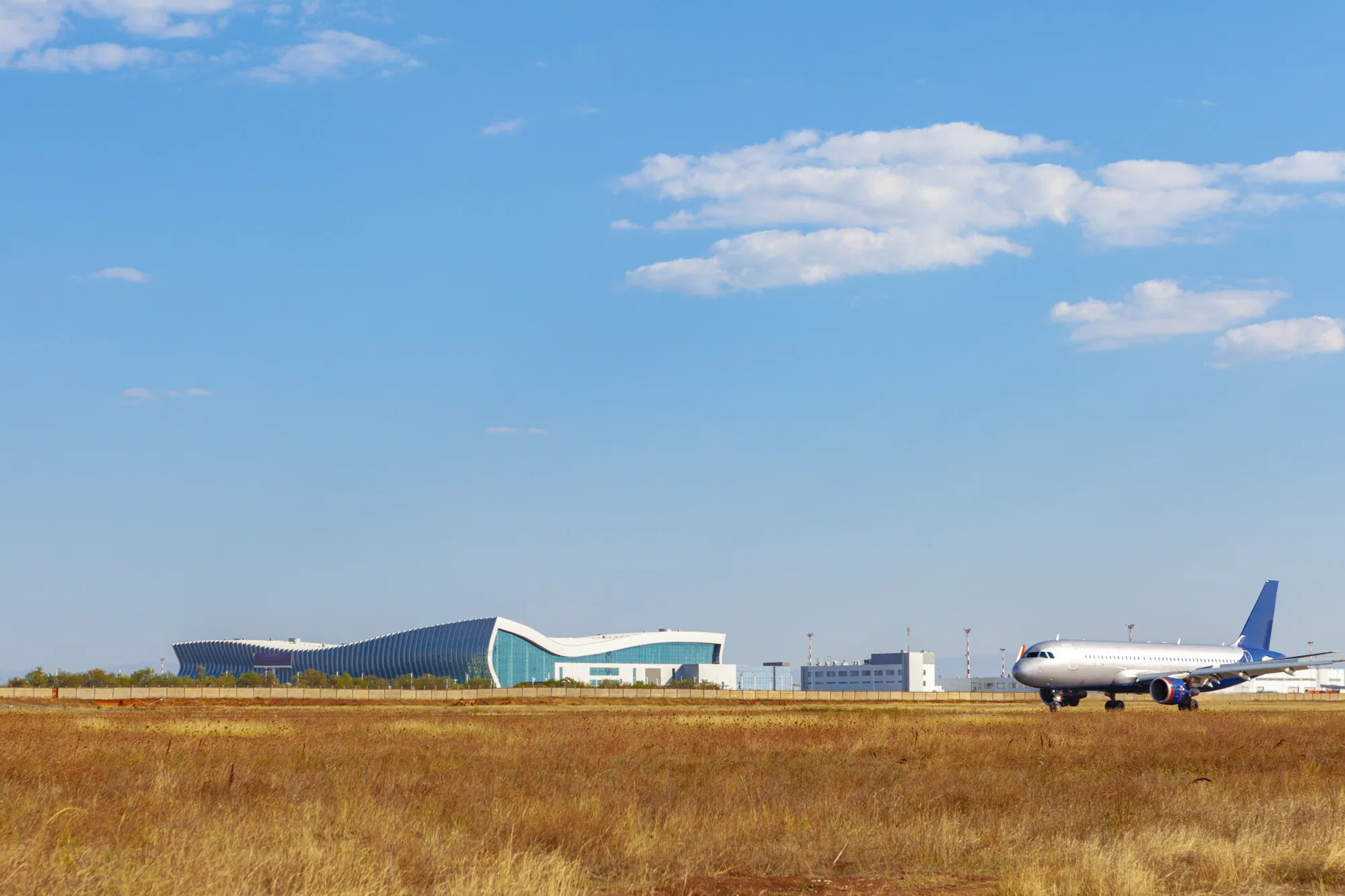 Putnički avion na pisti ispred moderne zgrade aerodromskog terminala, pod vedrim nebom sa oblacima
