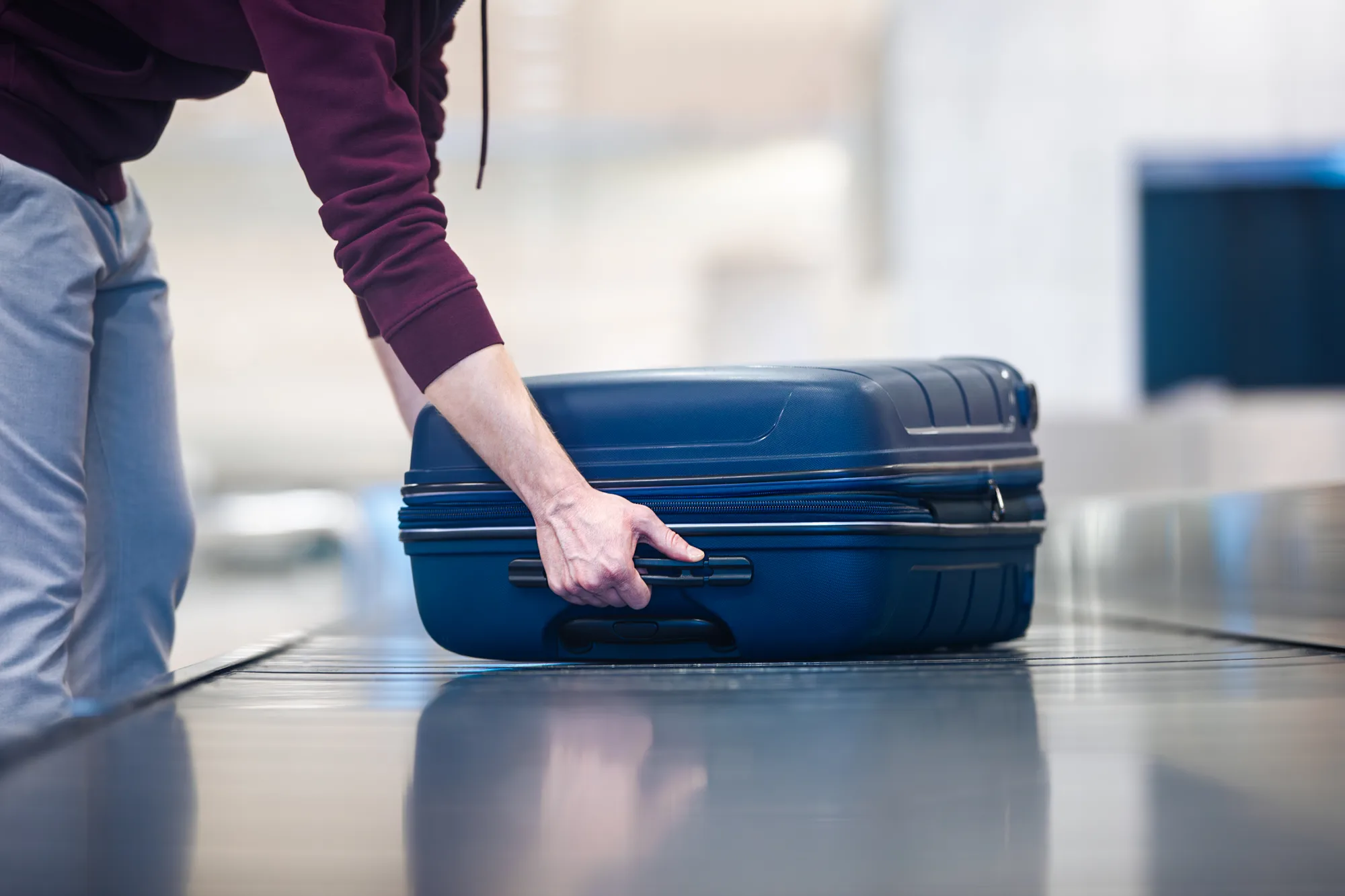 Putnica stavlja plavi kofer na traku za predaju prtljaga na aerodromu