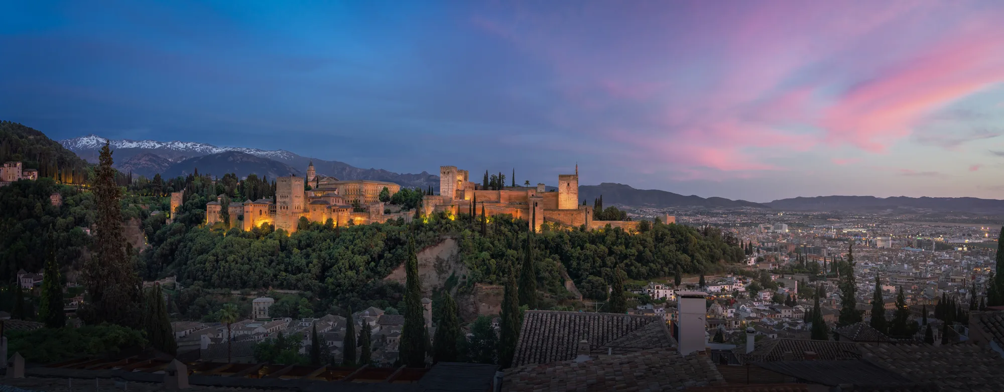 Osvetljena Alhambra na brdu iznad Granade u sumrak, sa snežnim vrhovima Sierra Nevade u pozadini